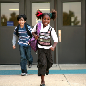 School building with two children running towards the camera excited about their accomodations