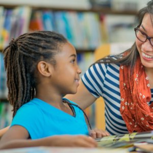 black child with long locs in a pony tail using effective communication skills talking to her asian american teacher who has long hair wearing glasses and a red flower scarf