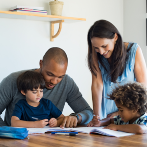 Black male with short haitcut is holding his son on his lap helping him with homework