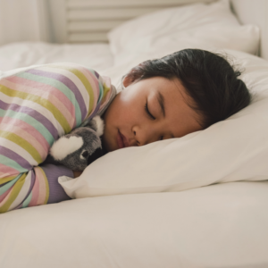 child with short haircur sleeping in bed with a bunny showing bedtime routines