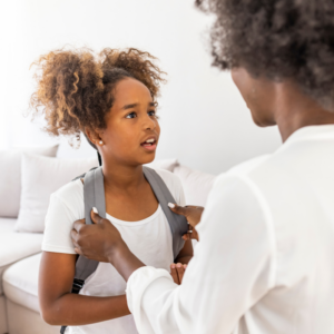 a child with curly pony tails wearing a white t-shirt and backpack looking at her mom as she get ready using morning routines 